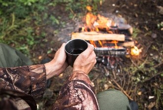 man drinking by campfire