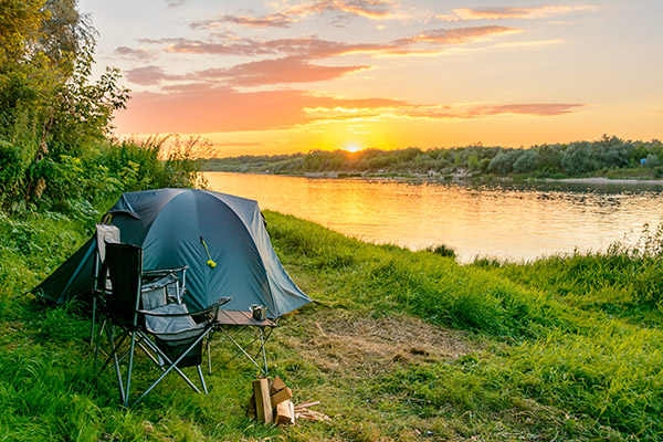 A tent, chair, and small pile of wood against the shore during a sunset.